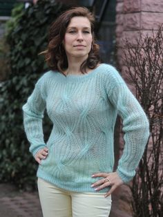 a woman standing in front of a brick building wearing a green sweater and tan pants