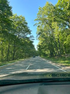 a car driving down a road next to lots of trees and grass on both sides of the road