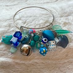 "4\" loaded charm bangle with blue and silver colored charms. There are clay, plastic, metal and wood and ceramic charms that were handmade by me. Some of these charms were picked up at stores in Maui during my 2016 trip, some were bought at Joann's and some were rescued from rummage sales. There are hearts and self made button charms. A bell, a shell, a spooky skull, happy little owl, and a cleansed evil eye charm for protection✨" Wood And Ceramic, Rummage Sale, Bun Hat, Wood Bracelet, Puff Stitch, Quality Hats, How To Make Buttons, Self Made, Evil Eye Charm