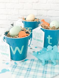 three blue buckets filled with eggs and dinosaur toys on a table next to a thank you sign