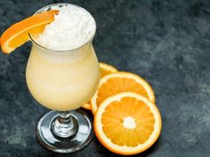 an orange drink with whipped cream and garnish on the rim next to sliced oranges