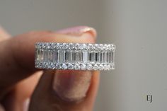 a woman's hand holding a ring with three baguetts on it and two rows of diamonds around the band