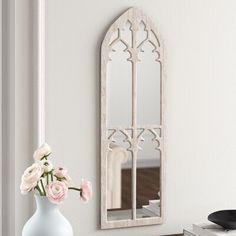 a white vase with flowers in it next to a mirror and record player on a table