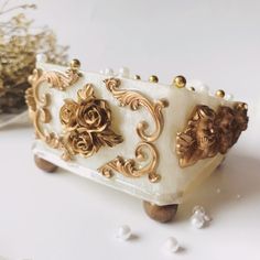 a white and gold decorated cake sitting on top of a table next to some flowers