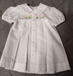 This is a traditional baby dress.  It is made from white cotton baptist.  The front yoke is hand embroidered with bunnies and flowers.  The dress has a peter pan collar, the front and back have pleats.  The closure is down the front with 5 snaps.  On top of the snaps are 1/4 inch buttons giving it a button look but much easier to close.  There is lace below the yoke.  The sleeves are puffed with elastic at the opening.  The side seams are French seams.  This dress is a size 6 months, 18-22 pound Embroidered Fitted Baptism Dress For Summer, Fitted Embroidered Baptism Dress For Summer, Fitted Embroidered Baptism Dress For Spring, Fitted Embroidered Spring Baptism Dress, Spring Baptism Dress Embroidered And Fitted, Spring Embroidered Fitted Baptism Dress, Summer Embroidered Fitted Baptism Dress, Spring Baptism Dress With Smock Detail, Fitted Baptism Dress With Embroidered Short Sleeves