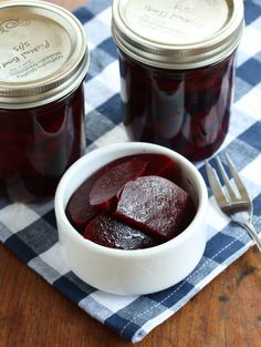 two jars of beets sitting on top of a blue and white checkered table cloth