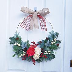 a wreath hanging on the front door with holly and red flowers, berries and pine cones