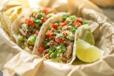 three tacos with meat, tomatoes and cilantro on paper wrapper next to chips