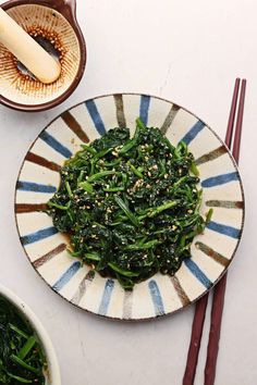 a plate with greens and chopsticks next to it on a white tablecloth