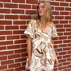 Featuring a brown tropical print set on a white cotton fabrication, this top is sure to keep you looking fab and feeling comfy all season long. The tiered design coupled with the loose short sleeves creates a flowy and beautifully feminine silhouette. With an open back and adjustable neck ties, this versatile tunic transitions from Saturday night to Sunday morning with ease!  Whether you wear this dress around town or to brunch with the girls, you're guaranteed to look and feel like a bohemian q Summer Tiered Tops For Vacation, White Tiered Tops For Summer, Casual Tiered Tops For Vacation, White Tiered Summer Top, White Tiered Casual Tops, Casual Tiered Tops With Floral Print, Summer Brown Tops With Floral Print, Brown Printed Tops For Vacation, Casual Tiered Tops For The Beach