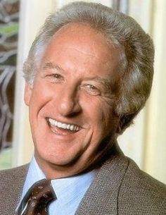 an older man wearing a suit and tie smiling for the camera with his eyes closed