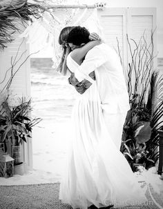 a bride and groom kissing in front of an open door with the ocean behind them