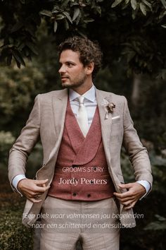 a man wearing a suit and tie standing in front of trees with his hands on his hips