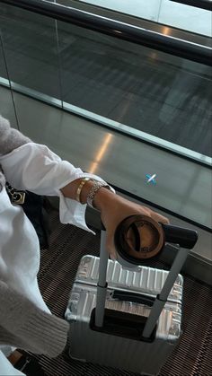 a woman sitting on top of a metal chair next to an airport luggage bag and looking out the window