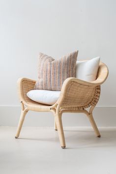 a wicker chair with two pillows on it and a white wall in the background