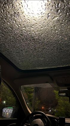 the inside of a car with raindrops on the windshield and dash light in the background