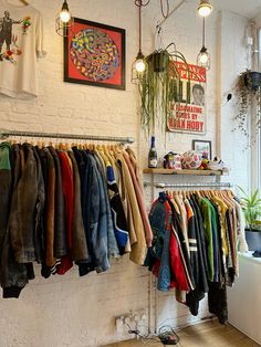 a clothing rack filled with lots of clothes next to a wall mounted planter and potted plants