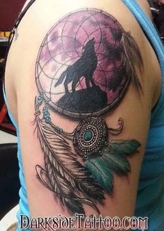 a woman's arm with a wolf and dream catcher tattoo on the back of her shoulder