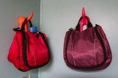 two purses are hanging on the wall with toothbrushes in them and one is red