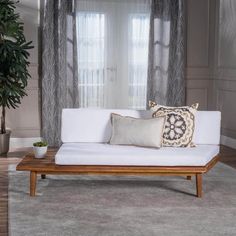 a white couch sitting in front of a window next to a potted plant on top of a wooden table