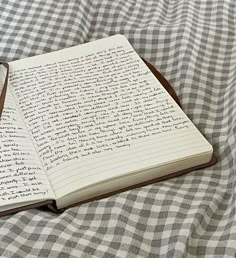 an open notebook sitting on top of a bed covered in checkered sheets and writing