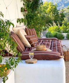 an outdoor seating area with pillows and hats on the bench, surrounded by greenery