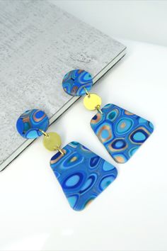 two blue and gold earrings sitting on top of a white table next to a book