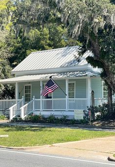 a white house with an american flag on the front porch and trees in the background