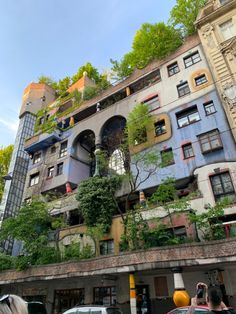 an apartment building with many windows and plants growing on it's side, surrounded by parked cars