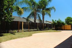 an empty backyard with palm trees in the back ground and a fenced in area