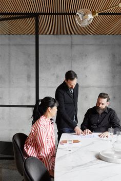 three people are sitting at a table and one is looking at something on the paper