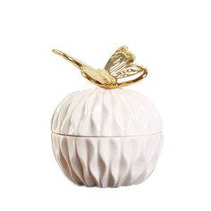 a small white vase with a gold butterfly on it's top, sitting on a white surface