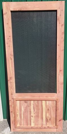 a wooden frame with a black screen on the front and side of it, sitting in front of a green door