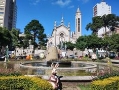 a statue of a rabbit in front of a fountain with flowers and trees around it