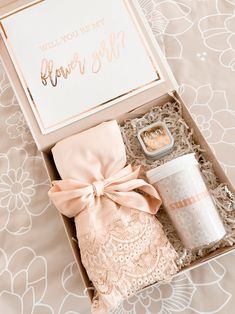 an open box with a cup, candle and napkin in it sitting on a bed