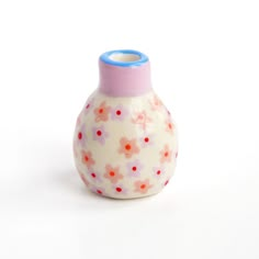 a small white vase with pink and red flowers on it's side, against a white background