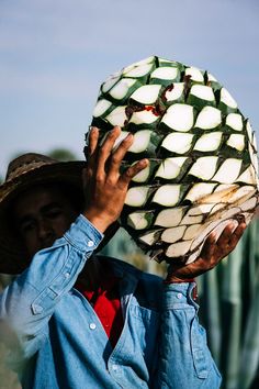 a man wearing a hat holding up a large piece of food to his face with both hands