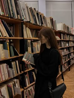 a woman standing in front of a bookshelf holding a book and looking at it