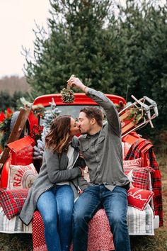 a man and woman sitting on the back of a red pickup truck with christmas decorations