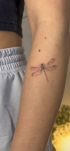 a woman's arm with a small dragonfly tattoo on it