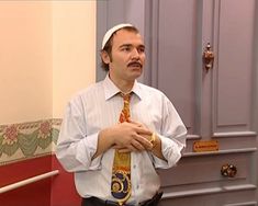 a man wearing a white shirt and tie standing in front of a door with his hands folded