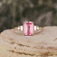 a pink tourmaline and diamond ring sitting on top of a rock