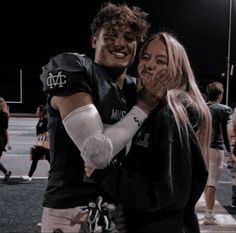 a man and woman hugging each other on the football field at night with people in the background