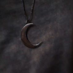 a crescent moon pendant hangs from a chain on a dark background, with the moon visible in the distance