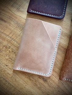 three different colored leather wallets on a wooden table