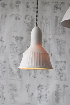 two white lamps hanging from a ceiling in front of wallpaper