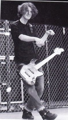 a young man holding a guitar while standing next to a chain link fence with his hands in the air