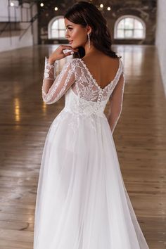 a woman in a white wedding dress standing on a wooden floor with her back to the camera