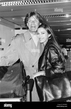 a man and woman standing next to each other at an airport, smiling for the camera