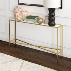 a gold console table with books and candles on it in front of a white wall